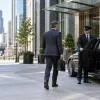 Male chauffeur greeting a business traveler beside an unbranded black sedan